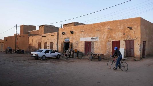Man on Bicycle Riding Past Old Buildings in Atar - Mauritania